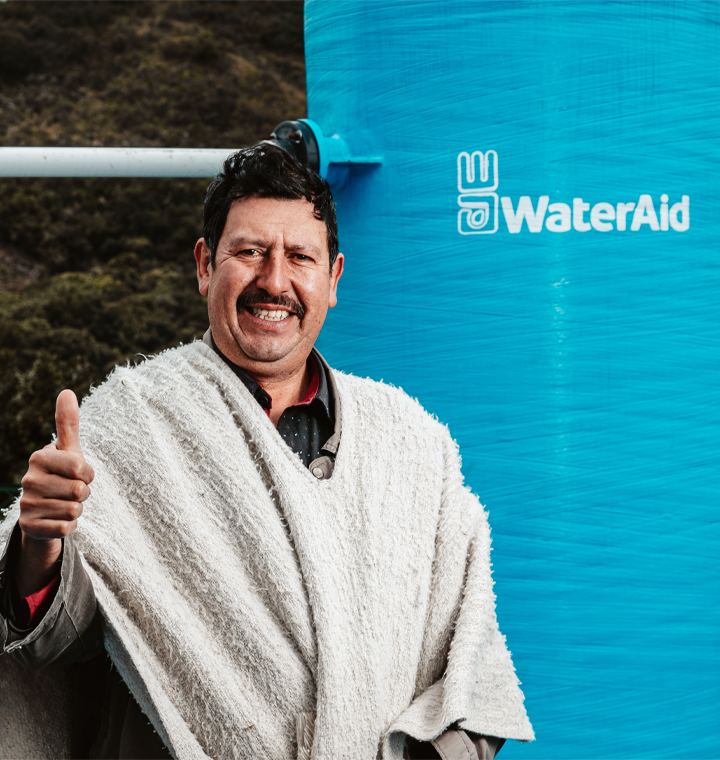 Man holding a thumbs up next to a WaterAid sign