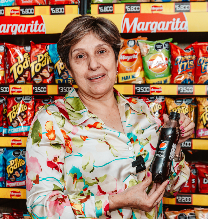 Woman holding Pepsi bottle in front of shelves holding PepsiCo products